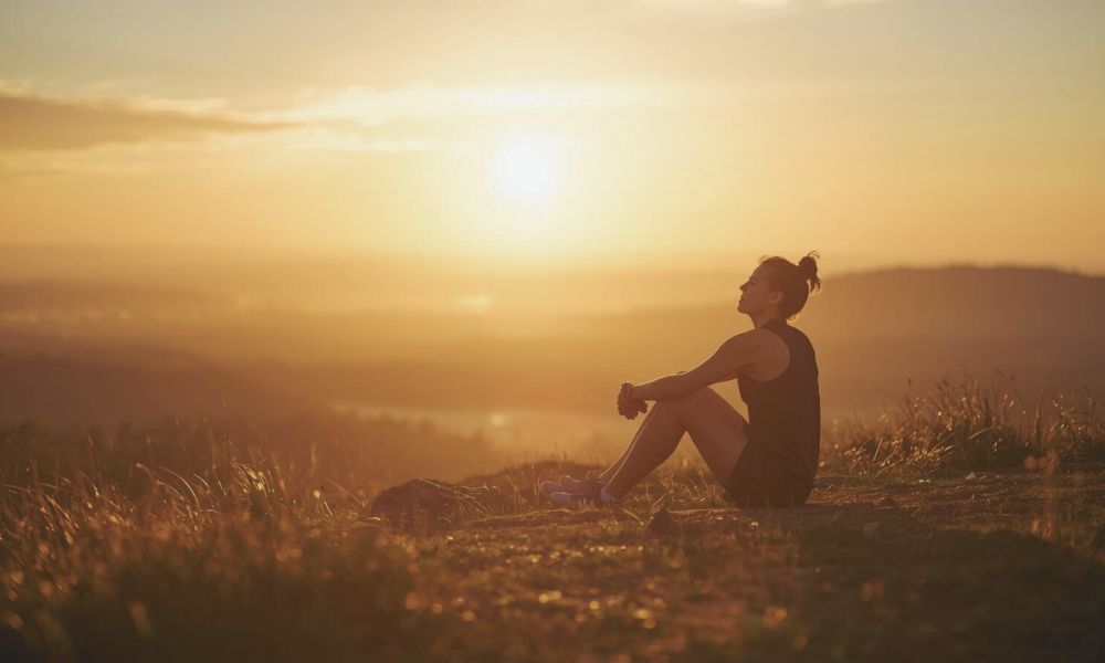 Runner sitting peacefully on a quiet hilltop at sunset with eyes closed, bathed in warm golden light, symbolizing emotional healing and calm after a reflective run.